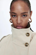 Women's beige short trench coat with belt, made of lightweight fabric, featuring a classic double-breasted design and side…