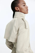 Women's beige short trench coat with belt, made from lightweight fabric, featuring a classic double-breasted design and side…