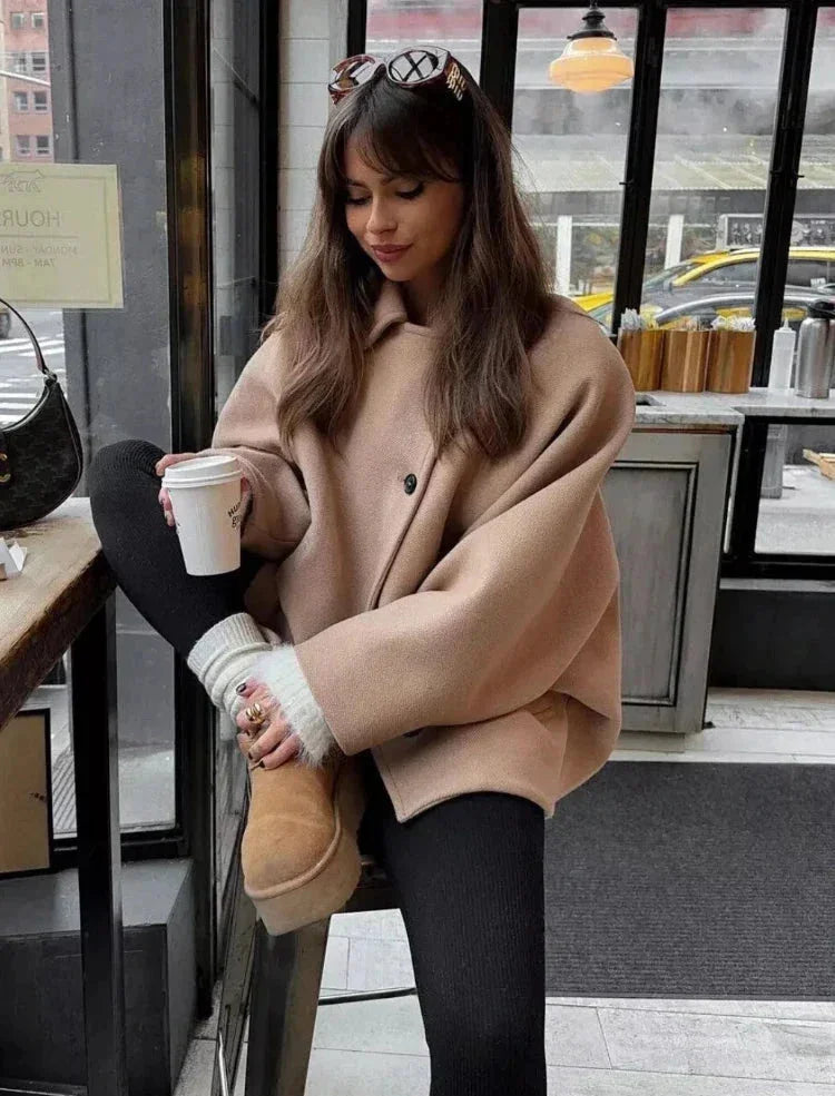 Women's beige oversized coat with a vintage-inspired design, featuring soft fabric, wide lapels, and large front pockets.