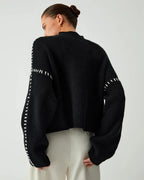 Women's black sweater made of soft fabric, featuring distinctive white stitch detailing for added visual interest.
