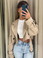 Women's cropped beige trench coat featuring long sleeves, made from lightweight fabric with a classic double-breasted design.
