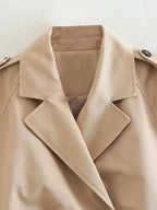 Women's cropped beige trench coat featuring long sleeves, a belted waist, and lightweight fabric for a tailored look.