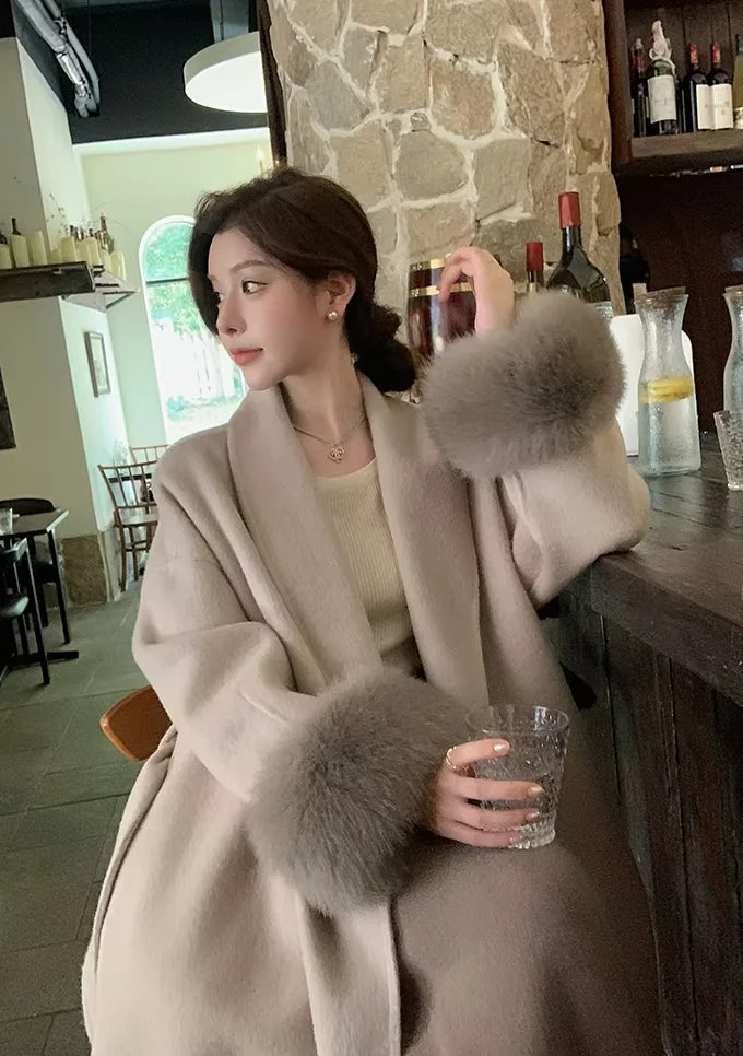 Women's long belted coat featuring faux fur cuffs, crafted from warm fabric for style and comfort in cooler weather.