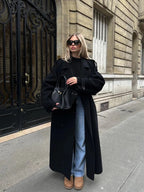 Women's long black coat made from soft fabric, featuring a belt, wide lapels, and a tailored silhouette for a stylish look.