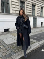 Women's long black coat with belt, wide lapels, crafted from soft wool blend for warmth and style in cooler weather.