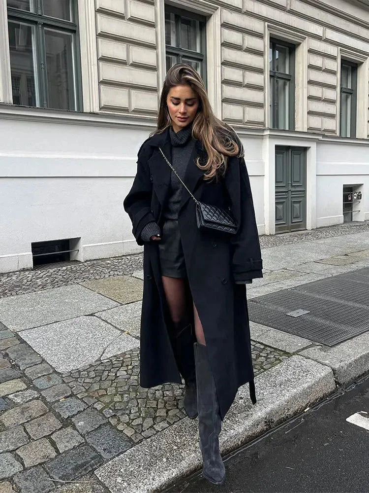 Women's long black coat with belt, wide lapels, crafted from soft wool blend for warmth and style in cooler weather.
