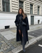 Women's long black coat made of durable wool, featuring a belted waist and wide lapels for a chic, tailored look.