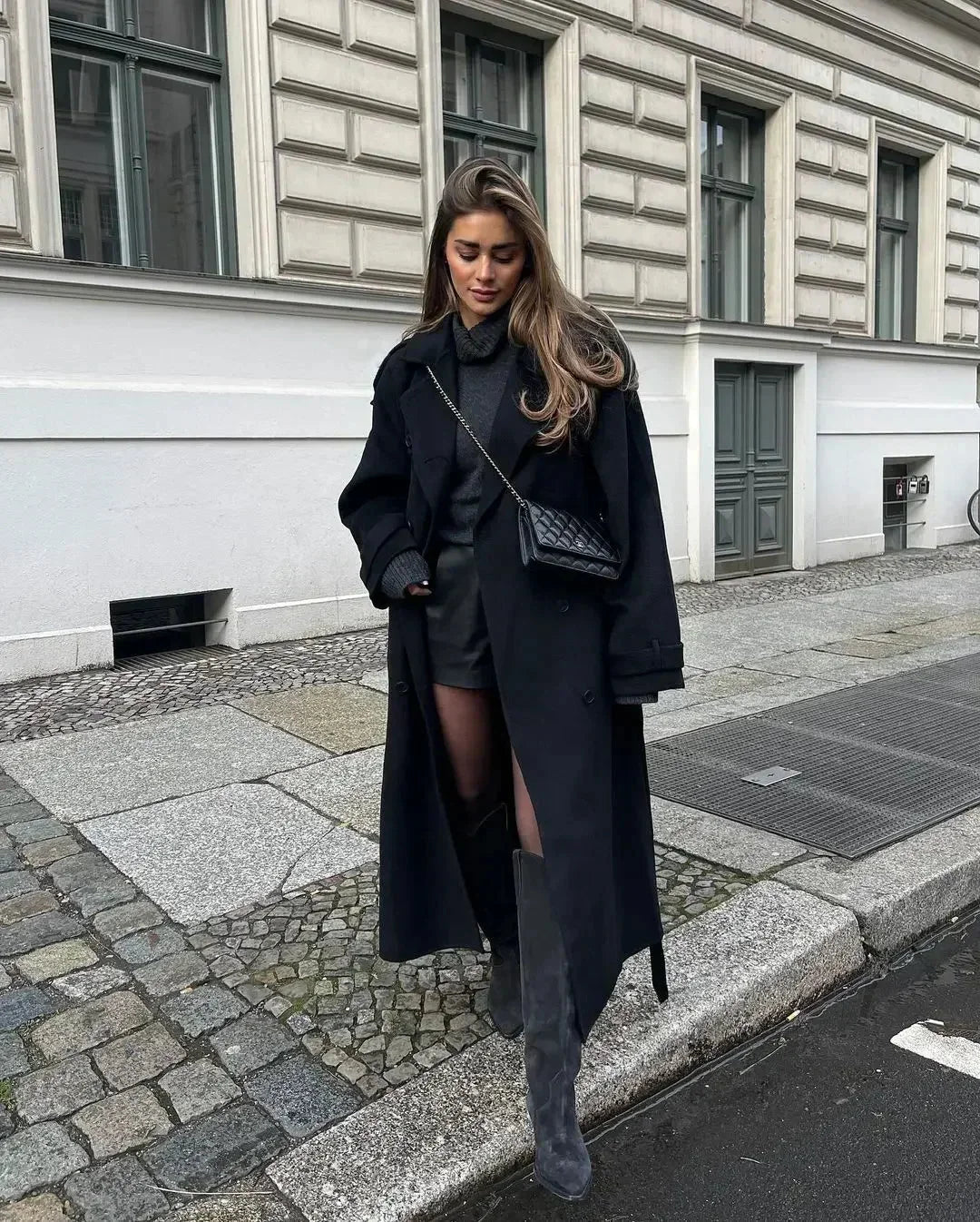 Women's long black coat made of durable wool, featuring a belted waist and wide lapels for a chic, tailored look.