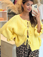Women's open-front yellow cardigan made of soft knit fabric, featuring bow tie details on the cuffs for a charming touch.